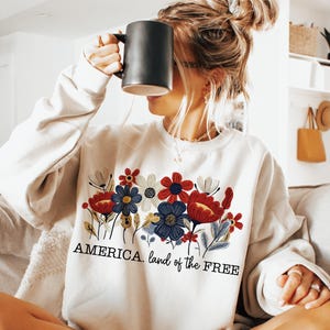 May include: A white sweatshirt with a floral design and the text "AMERICA. land of the FREE".