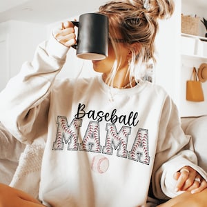May include: White sweatshirt with the text "Baseball Mama" in black lettering with red stitching around the letters. A baseball graphic is below the text.