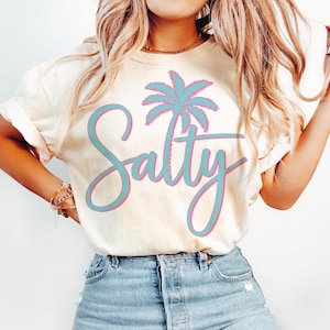 May include: A white t-shirt with a blue palm tree and the word "Salty" in pink and blue lettering.
