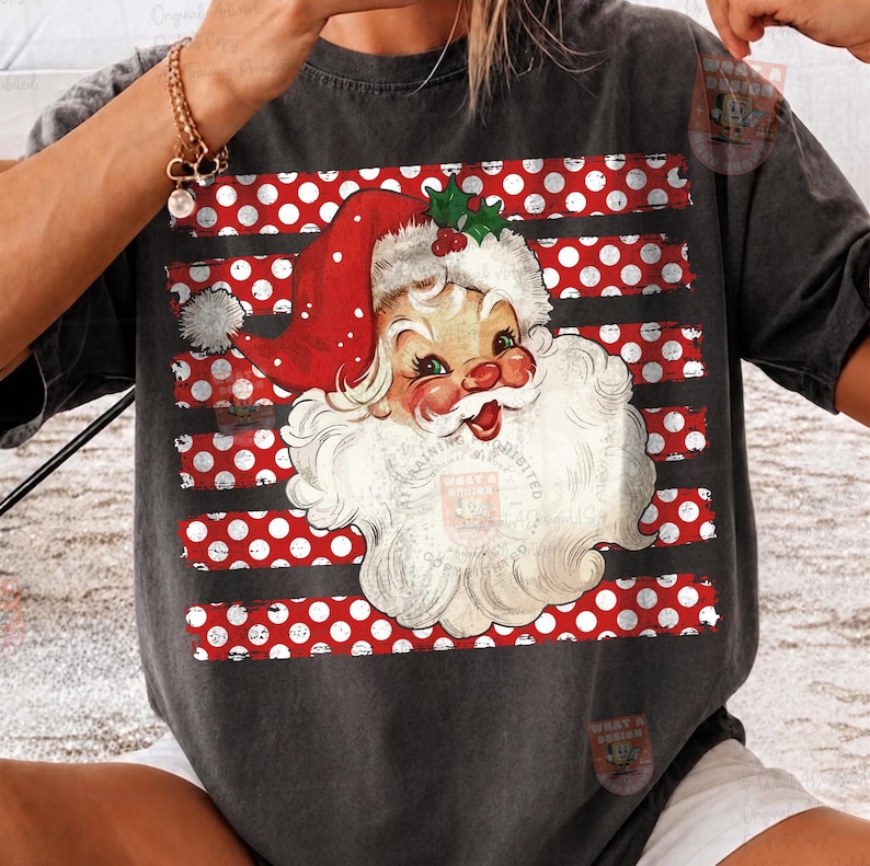 May include: A charcoal gray t-shirt featuring a graphic of a vintage-style Santa Claus face with a red hat and white beard. The design is layered over a background of horizontal red stripes with white polka dots across the center of the shirt.