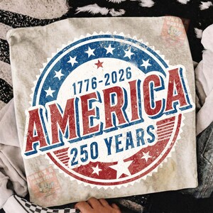 May include: A light-colored pillow with a distressed graphic celebrating 250 years of America. The design features a red, white, and blue circular emblem with the text "AMERICA" and the years "1776-2026".