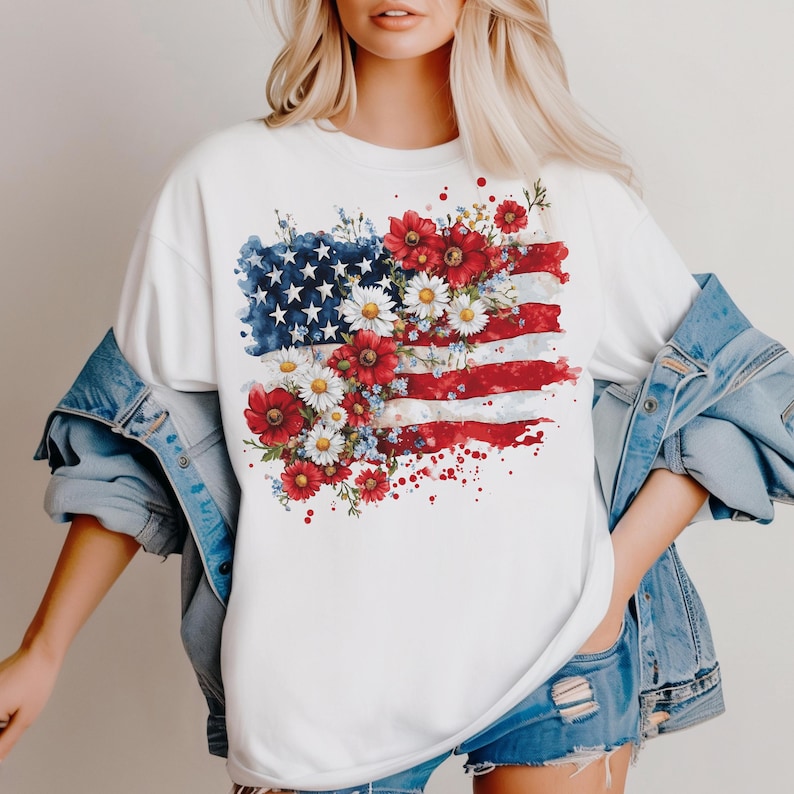 May include: White t-shirt with a watercolor design of the American flag with red, white, and blue flowers.