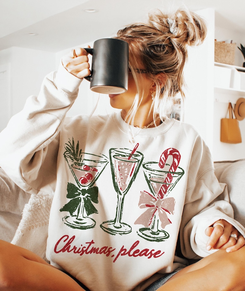May include: Cream-colored sweatshirt with a festive cocktail design. The graphic features three martini glasses with red and green accents, and a candy cane. The text "Christmas, please" is printed in red.