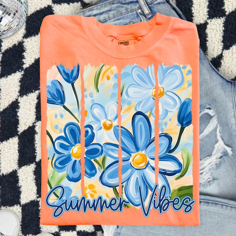 May include: A peach-colored t-shirt with a graphic of blue flowers and the text "Summer Vibes" printed on the front.