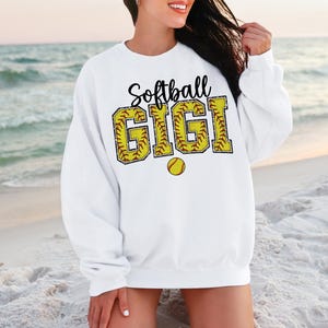 May include: White sweatshirt with the text "Softball Gigi" in black letters with a yellow softball graphic.