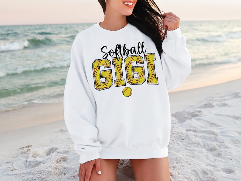 May include: White sweatshirt with the text "Softball Gigi" in black letters with a yellow softball graphic.