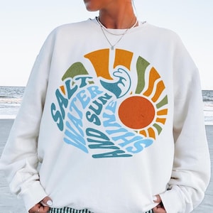 May include: White sweatshirt with a colorful graphic design featuring a sun, waves, and the text "Salt Water and Sunshine" in a retro font.