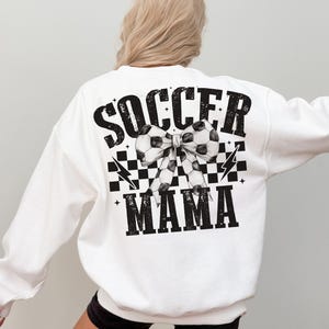 Puede incluir: Sudadera blanca con texto negro que dice "Soccer Mama" con un patr&oacute;n de cuadros blanco y negro y un lazo de bal&oacute;n de f&uacute;tbol blanco y negro.