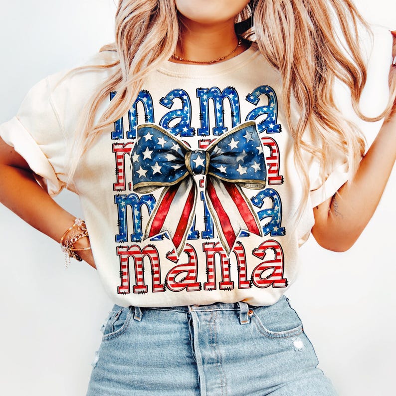 May include: Cream-colored t-shirt with the word "Mama" in blue and red, with a patriotic bow graphic. The bow features a blue star pattern and red and white stripes, evoking an American theme.