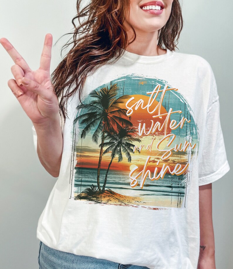 May include: White t-shirt with a graphic print of a sunset over the ocean with palm trees and the text "salt water and sun shine".