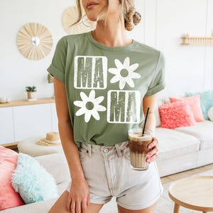 Peut inclure: Un t-shirt vert avec un motif graphique blanc qui dit "Mama" avec des fleurs dans le design.