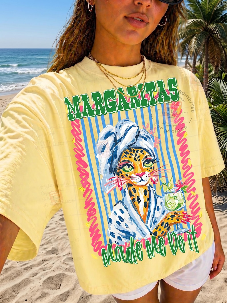 Pu&ograve; includere: T-shirt giallo con la scritta "Margaritas Made Me Do It". La grafica presenta un leopardo con un asciugamano e un cocktail. Il design include strisce blu e dettagli rosa.
