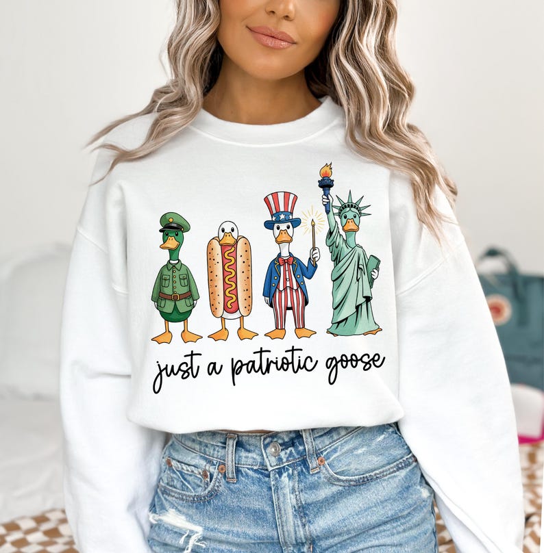 May include: White sweatshirt with a graphic of four cartoon geese dressed as patriotic symbols: a soldier, a hot dog, Uncle Sam, and the Statue of Liberty. The text "just a patriotic goose" is written below the geese.