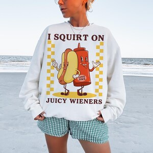 May include: White sweatshirt with a graphic of a hot dog and ketchup bottle with the text "I squirt on juicy wieners".