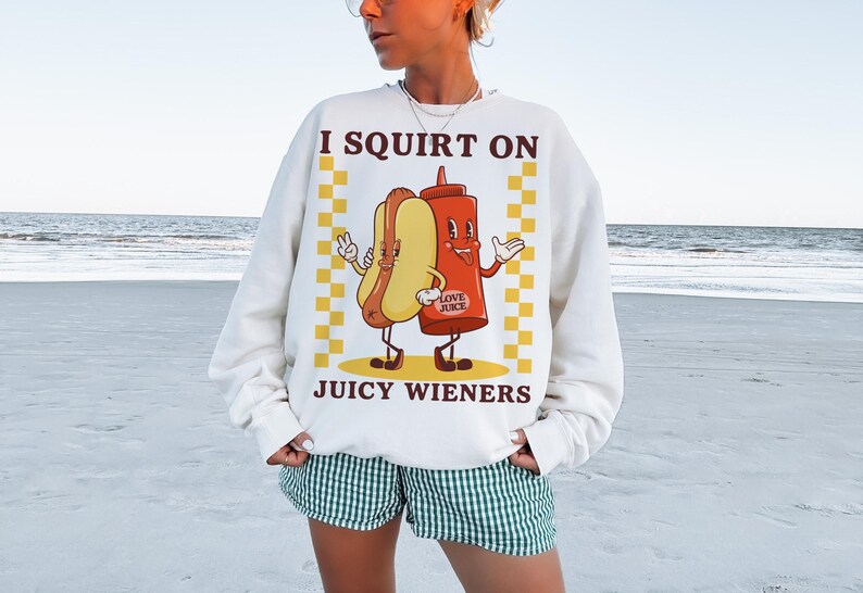 May include: White sweatshirt with a graphic of a hot dog and ketchup bottle with the text "I squirt on juicy wieners".