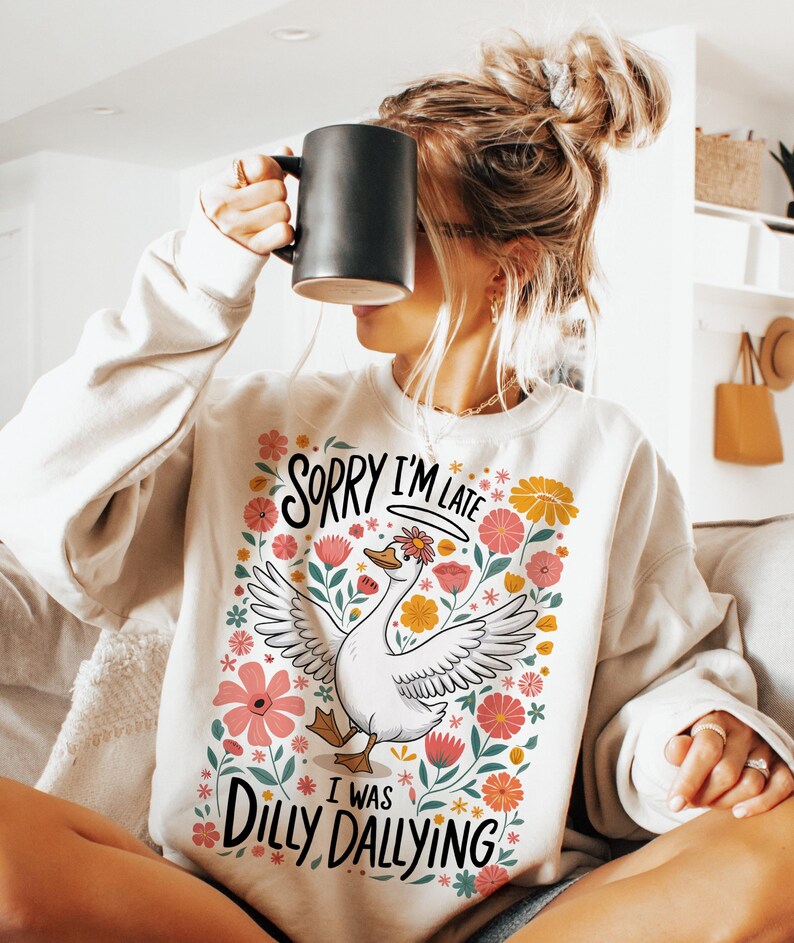 May include: White sweatshirt with a floral design and a goose illustration. The text on the sweatshirt reads "Sorry I'm Late I Was Dilly Dallying".