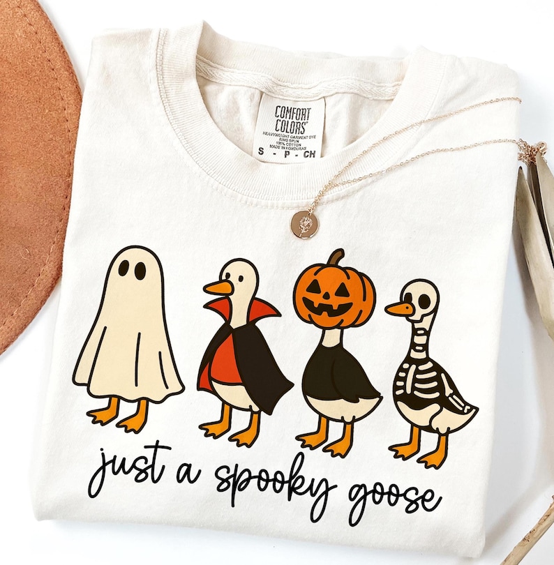 Digital Just a Spooky Goose Halloween PNG design featuring geese dressed in ghost, pumpkin, and witch costumes in a row. Shown on a t-shirt mockup.