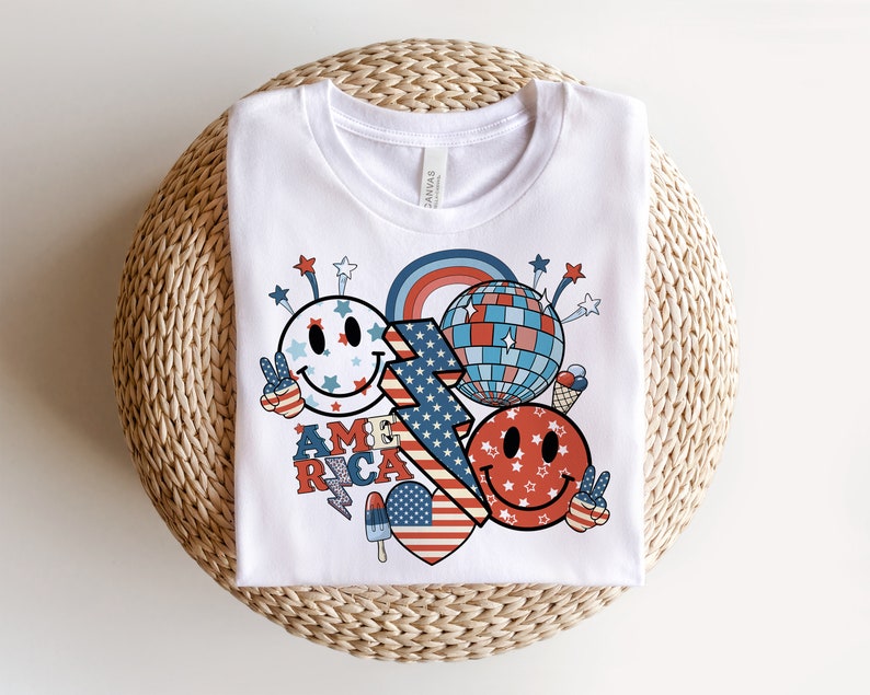 May include: White t-shirt with a red, white and blue graphic design featuring a smiley face, a disco ball, and the word "AMERICA".
