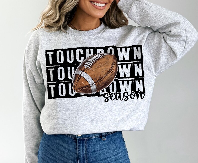 Op de afbeelding: Grijs sweatshirt met een zwart-witte afbeelding van een voetbal en de tekst "Touchdown season".