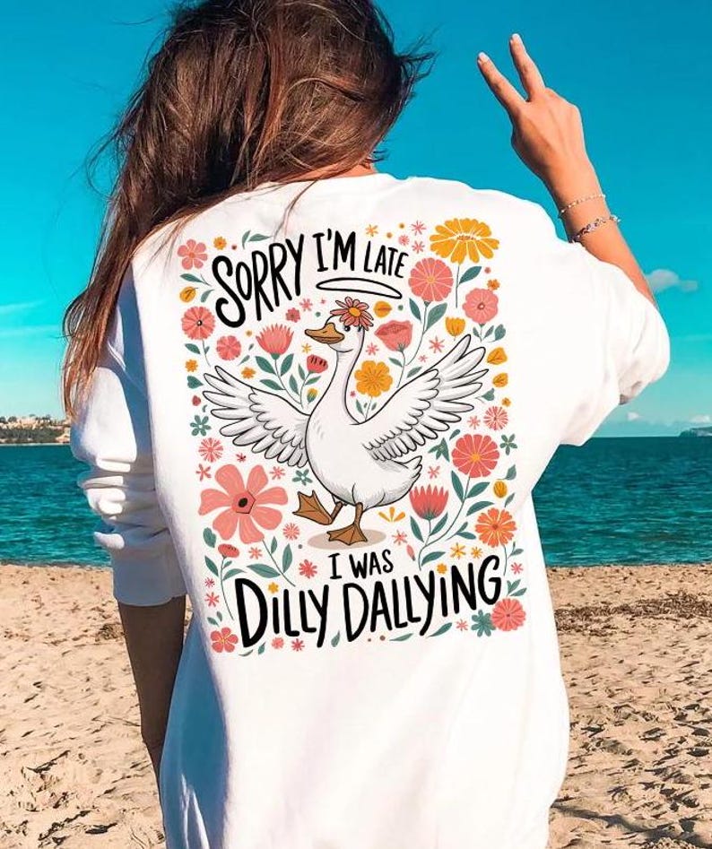 May include: White t-shirt featuring a floral design and a cartoon goose. The text on the shirt reads "Sorry I'm late I was dilly dallying."