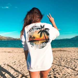 May include: White sweatshirt with a graphic print of a sunset over a beach with palm trees and the text "Summer Vibes".