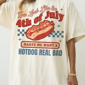 May include: A white t-shirt with a vintage-style graphic that says "You Look Like the 4th of July" with a hot dog illustration and the text "Makes me want a hotdog real bad".