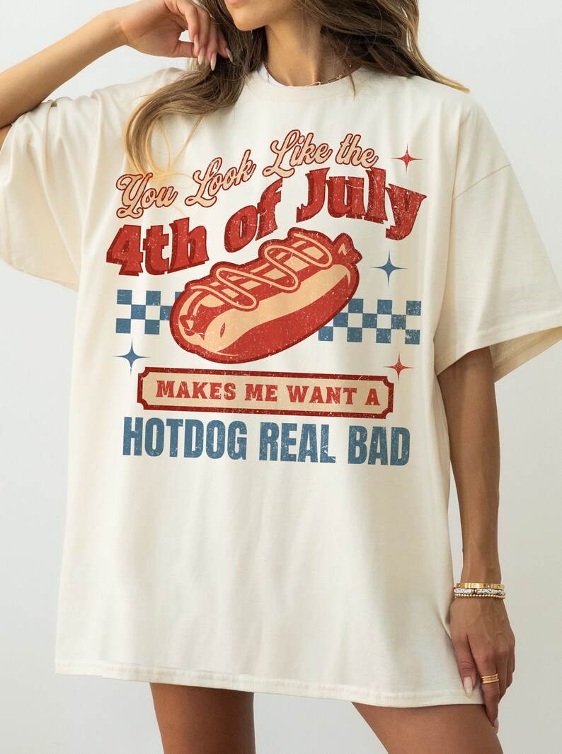 May include: A white t-shirt with a vintage-style graphic that says "You Look Like the 4th of July" with a hot dog illustration and the text "Makes me want a hotdog real bad".