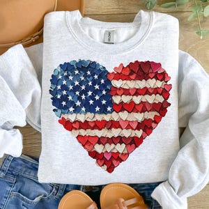 May include: A gray sweatshirt with a heart-shaped design made of small red, white, and blue hearts. The design resembles the American flag.