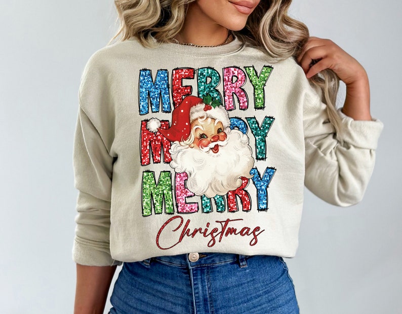 Op de afbeelding: Een beige sweatshirt met een feestelijk kerstontwerp. Het ontwerp bevat de woorden "Merry" drie keer herhaald in kleurrijke glitterletters, met een vintage illustratie van de kerstman in het midden. De woorden "Christmas" zijn in rode glitter geschreven onder de kerstman-illustratie.