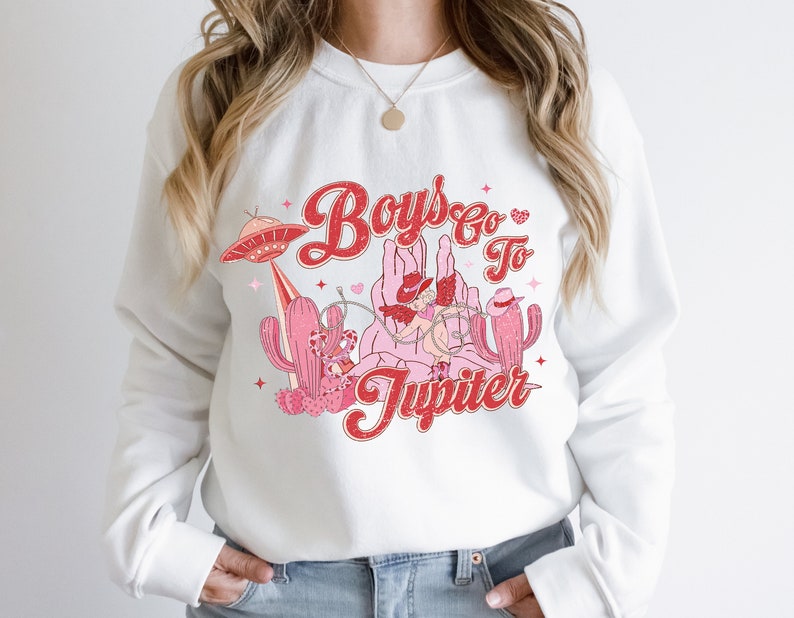 K&ouml;nnte beinhalten: Wei&szlig;er Pullover mit einem roten und rosafarbenen Grafikdesign mit dem Text "Boys Go To Jupiter" mit einem Cowboyhut, einem Kaktus und einem UFO.
