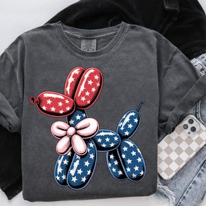 May include: A dark gray t-shirt with a red, white, and blue balloon dog graphic. The balloon dog is shaped like a dachshund and has a bow.