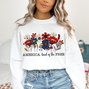 May include: White sweatshirt with a red, white, and blue floral design and the text "AMERICA. land of the FREE".