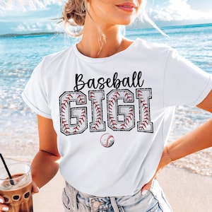 May include: White t-shirt with black text that reads "Baseball Gigi" with a baseball graphic design. The letters are outlined in red and white.