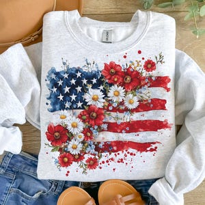 May include: A gray sweatshirt with a watercolor design of an American flag with red, white, and blue flowers.