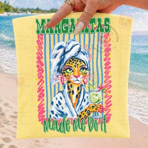 Pu&ograve; includere: Un telo mare giallo con un leopardo dei cartoni animati con un asciugamano e un accappatoio, che tiene in mano un cocktail. L'asciugamano ha le parole "Margaritas" e "Made Me Do It" in verde, con strisce blu e accenti rosa.