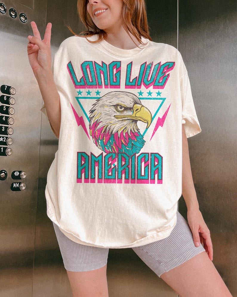 May include: A white t-shirt with a graphic of an eagle in a triangle with the text "Long Live America" in turquoise and pink.