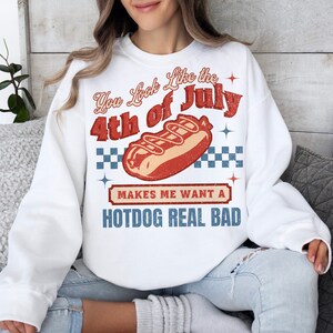 May include: White sweatshirt with a red, white, and blue graphic that says "You look like the 4th of July" with a hot dog illustration and the text "Makes me want a hotdog real bad".