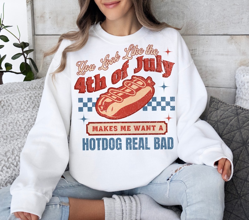 May include: White sweatshirt with a red, white, and blue graphic that says "You look like the 4th of July" with a hot dog illustration and the text "Makes me want a hotdog real bad".
