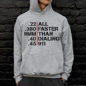 May include: A gray hooded sweatshirt with a black graphic print that reads ".22 ALL FASTER THAN DIALING 911". The text is separated by a red vertical line.