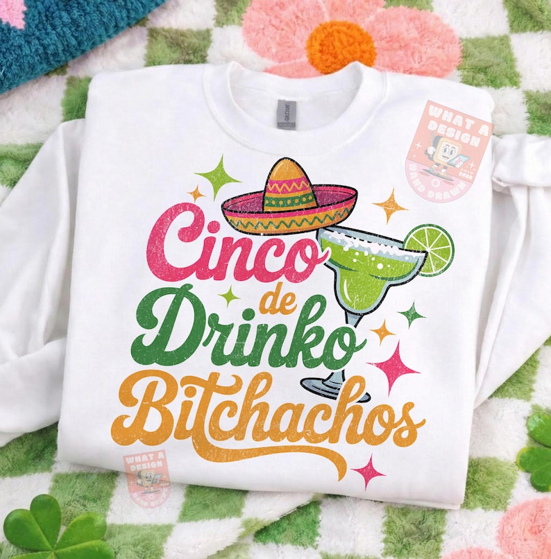 May include: White sweatshirt with a colorful Cinco de Mayo design. The graphic includes a sombrero, margarita, and the words "Cinco de Drinko Bitchachos" in pink, green, and orange. The design has a distressed, vintage look.