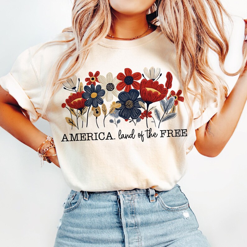 May include: A white t-shirt with a floral design in red, blue, and yellow. The text "AMERICA. land of the FREE" is printed below the flowers.