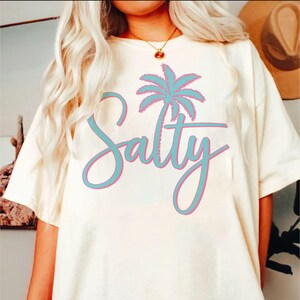May include: A white t-shirt with a blue palm tree and the word "Salty" in pink and blue lettering.