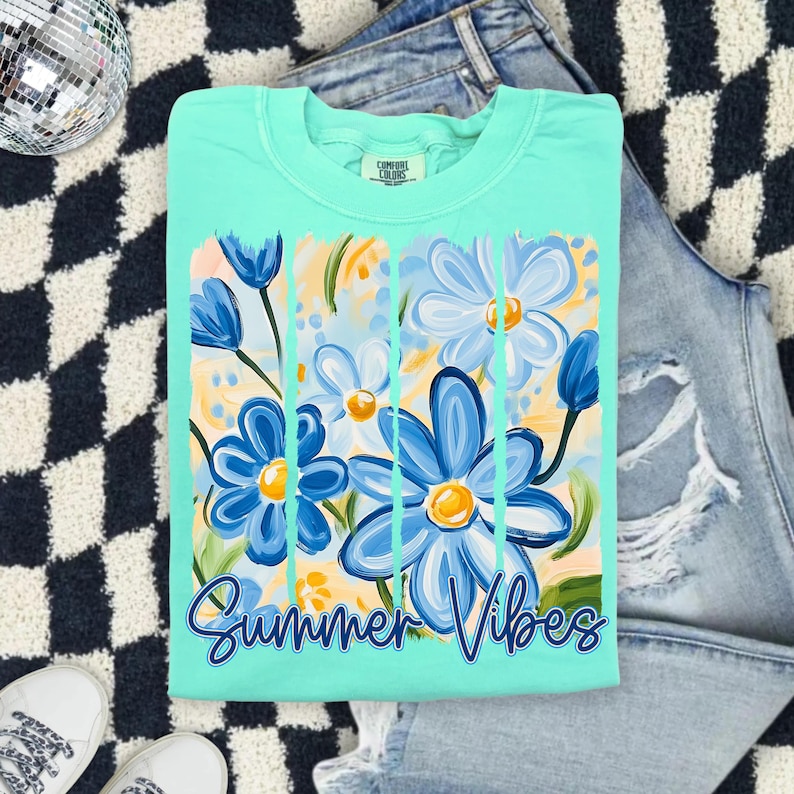 May include: A turquoise blue t-shirt with a graphic of blue and yellow flowers and the text "Summer Vibes".