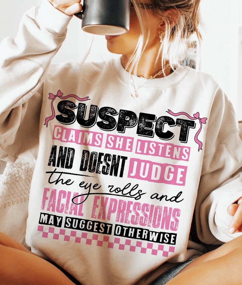 May include: A white sweatshirt with a black and pink graphic print that says "SUSPECT CLAIMS SHE LISTENS AND DOESNT JUDGE the eye rolls and FACIAL EXPRESSIONS MAY SUGGEST OTHERWISE".