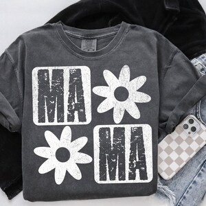 Peut inclure: Un t-shirt gris fonc&eacute; avec un motif graphique blanc. Le graphique pr&eacute;sente le mot "mama" dans une police de caract&egrave;res us&eacute;e, entour&eacute; de marguerites blanches stylis&eacute;es.