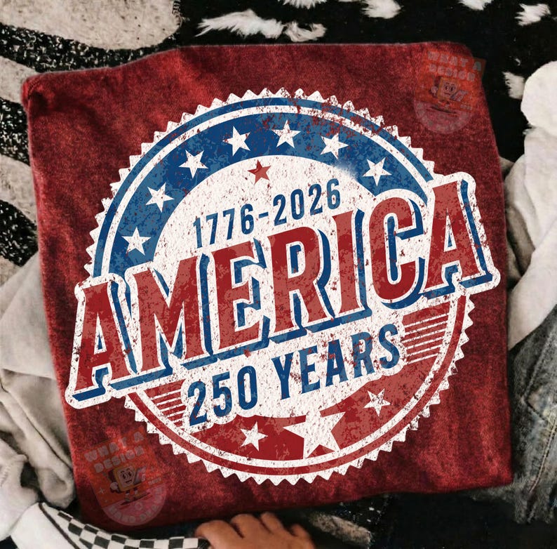May include: A red t-shirt featuring a distressed design celebrating 250 years of America. The design includes a blue and white circular emblem with stars, the text "AMERICA" in red and white, and the years "1776-2026".
