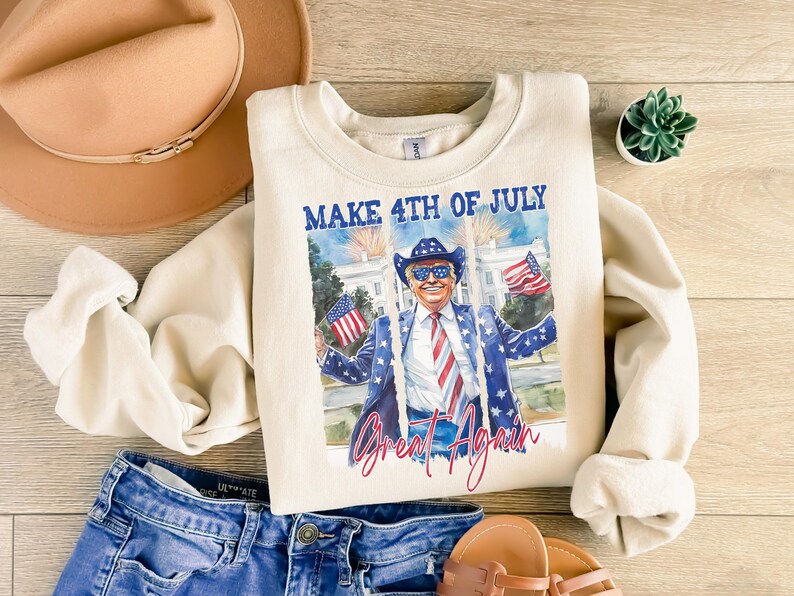 May include: A cream-colored sweatshirt with a graphic print of a man wearing sunglasses and a red, white, and blue tie. The text "Make 4th of July Great Again" is printed on the sweatshirt.