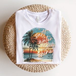 May include: White t-shirt with a graphic of palm trees, a sunset, and the text "salt water and sun shine".
