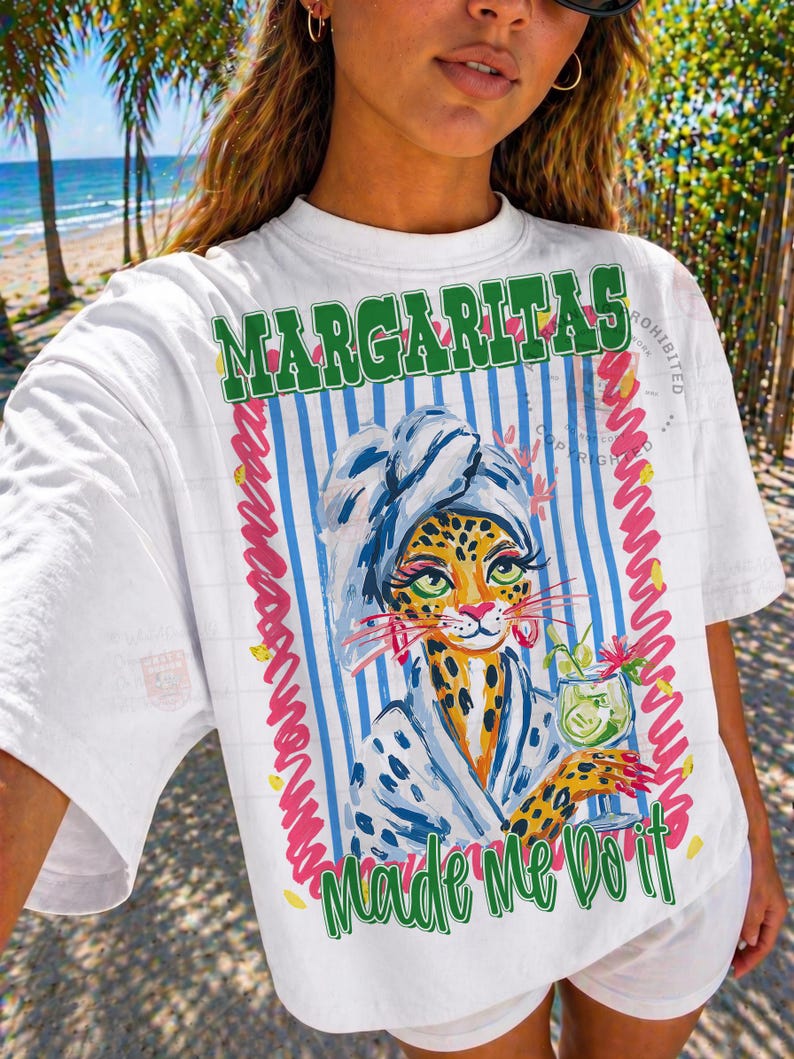 Pu&ograve; includere: T-shirt bianco con grafica colorata. La grafica presenta un leopardo con un accappatoio da spa e un cocktail, con le parole "Margaritas Made Me Do It" in testo verde e giallo. Lo sfondo ha strisce blu e bianche.