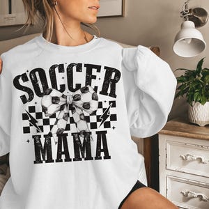 Puede incluir: Sudadera blanca con texto negro que dice "Soccer Mama" con un patr&oacute;n de cuadros blanco y negro y un lazo de bal&oacute;n de f&uacute;tbol.
